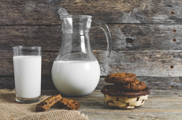 Biscotti di farina d'avena con gocce di cioccolato brocca e bicchiere di latte in legno rustico sfondo Cena di campagna