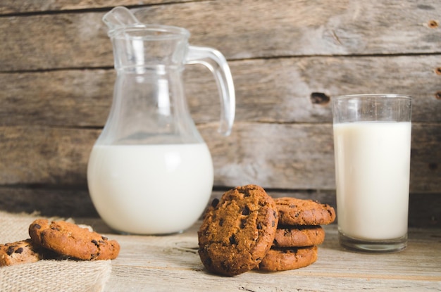 Biscotti di farina d'avena con gocce di cioccolato brocca e bicchiere di latte in legno rustico sfondo Cena di campagna