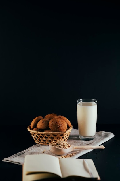 Biscotti di farina d'avena con un bicchiere di latte su un tovagliolo su sfondo nero Il concetto di una sana colazione