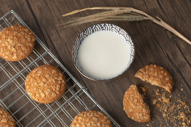 Biscotti di farina d'avena fatti in casa con semi e ciotola di latte fresco sulla tavola di legno