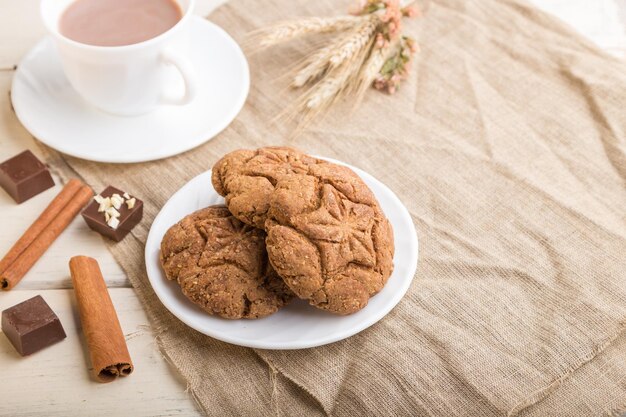 Biscotti di farina d'avena fatti in casa con una tazza di cacao su un tessuto di lino e uno sfondo di legno bianco. vista laterale, primo piano, messa a fuoco selettiva, copia spazio.