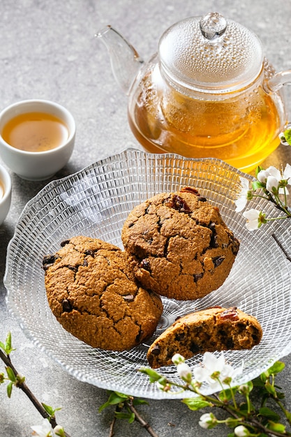 Biscotti di farina d'avena fatti in casa su un tavolo con rami di un albero in fiore e tè verde in una teiera di vetro.