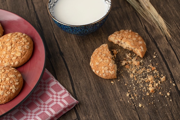 Biscotti di farina d'avena incrinati con semi e ciotola di latte fresco sulla tavola di legno