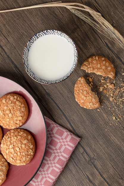 Biscotti di farina d'avena incrinati con semi e ciotola di latte fresco sulla tavola di legno