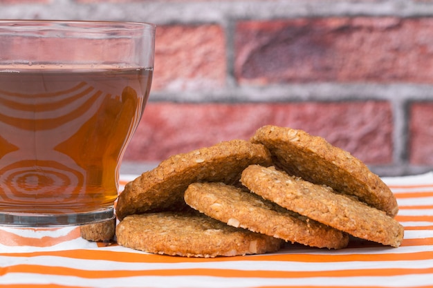 Biscotti di farina d'avena su tovagliolo a strisce bianche e arancioni accompagnati da un bicchiere di tè e un muro di mattoni sullo sfondo