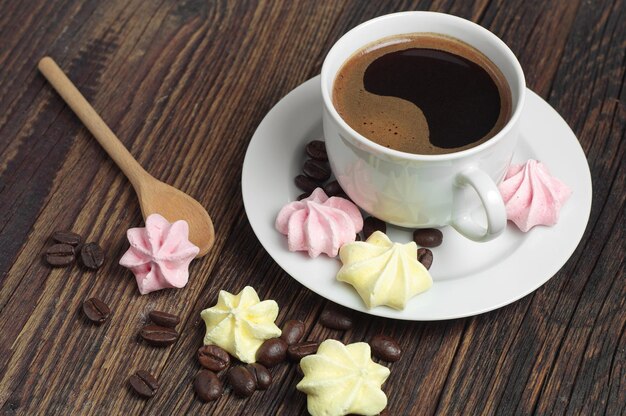 Biscotti di meringa colorati e tazza di caffè caldo su tavola di legno rustica