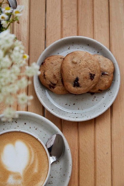 Biscotti di mirtillo rosso naturale senza zucchero sul piatto cappuccino in tazza di ceramica bianca su tavolo in legno vista dall'alto sfocato in primo piano Colazione estetica presso la terrazza del caffè all'esterno