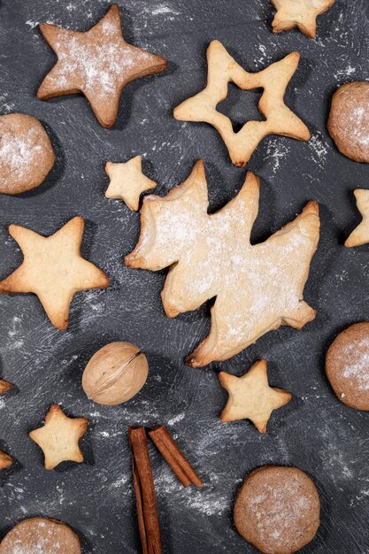 Biscotti di Natale fatti in casa di diverse forme, cannella, noci su sfondo nero da vicino.