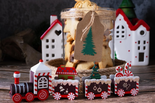 Biscotti di Natale fatti in casa in un barattolo di vetro con decorazioni per la tavola di Capodanno accanto a una locomotiva a vapore giocattolo e case