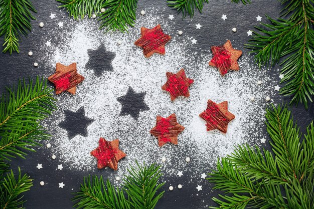 Biscotti di Natale fatti in casa stelle di cioccolato con scricchiolii di lampone con zucchero in polvere sul tavolo in ardesia con rami di pino