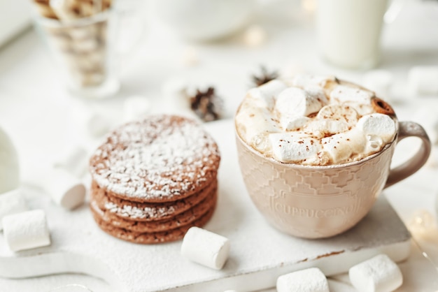 Biscotti di natale, latte, cacao, caramelle gommosa e molle, meringa su un piatto bianco vicino alla finestra