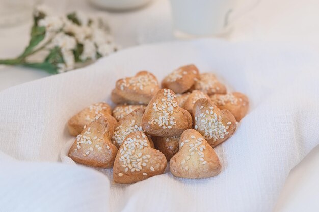 Biscotti di pasta frolla a forma di cuore decorati con semi di sesamo su fiori di campo bianchi da tavola e latte