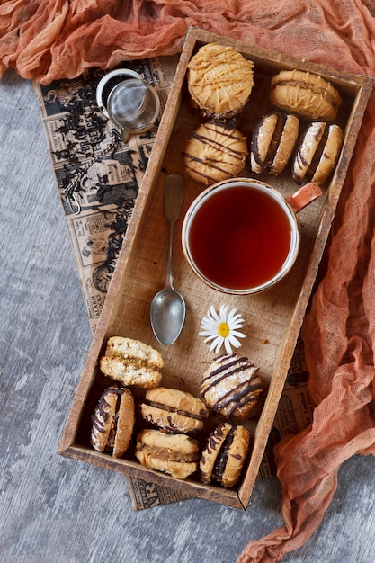 Biscotti di pasta frolla fatti in casa con un ripieno e una tazza di tè in una scatola di legno.