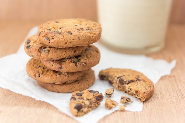 Biscotti di pepita di cioccolato e un bicchiere di latte su un fondo di legno