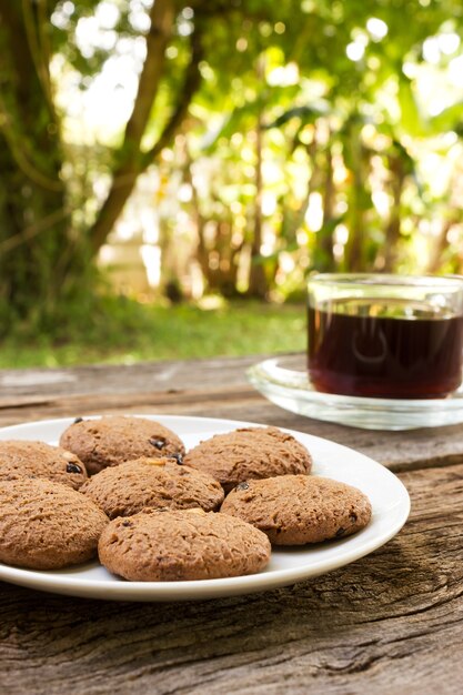 Biscotti di pepita di cioccolato sulla zolla bianca con un vetro di caffè.