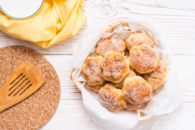 Biscotti di ricotta cosparsi di zucchero in un cestino e una tazza di latte su un tavolo di legno. copyspace