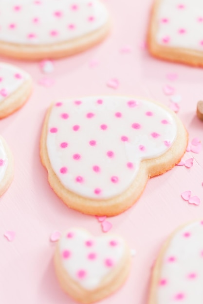 Biscotti di zucchero a forma di cuore decorati con glassa reale per San Valentino su sfondo rosa.