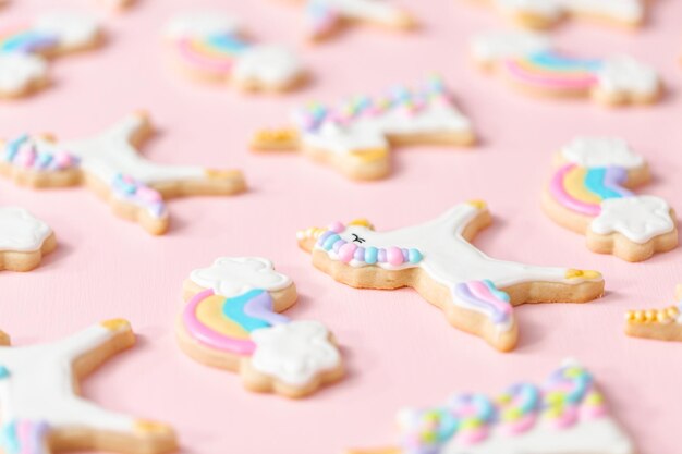 Biscotti di zucchero unicorno decorati con glassa reale su sfondo rosa.