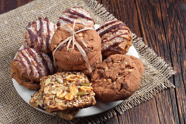 Biscotti differenti in piatto bianco su vecchio fondo di legno con tela da imballaggio