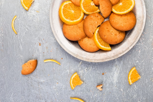 Biscotti e agrumi arancio su di piastra metallica su fondo grigio. Disteso