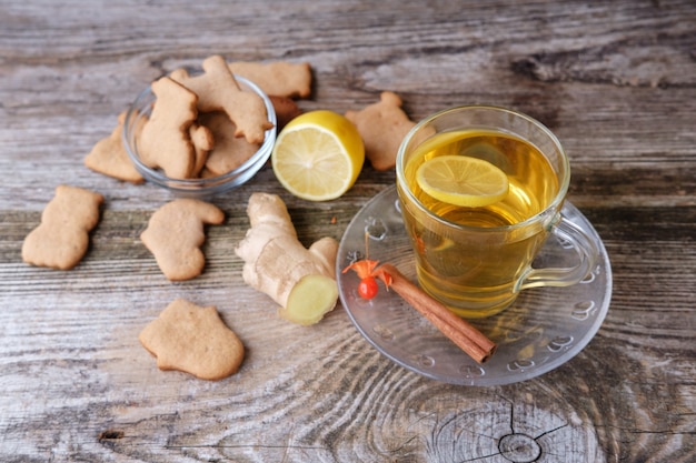 Biscotti fatti in casa allo zenzero a forma di animali, tè verde al limone in una tazza di vetro, cannella e physalis sul vecchio tavolo in legno