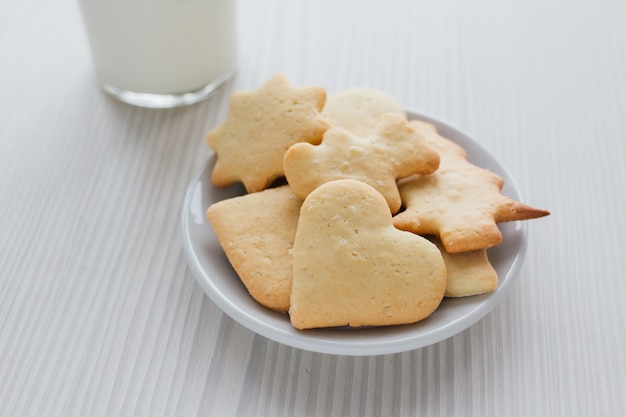 Biscotti fatti in casa appena sfornati e un bicchiere di latte su legno bianco