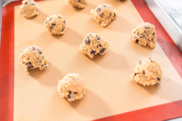 Biscotti fatti in casa con gocce di cioccolato scoop di pasta su una teglia con un tappetino in silicone.