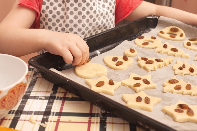 Biscotti fatti in casa con uvetta sul tavolo. Forme: cerchio, stella, albero, cuore. il bambino aiuta sua madre a cucinare