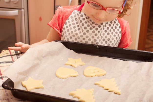 Biscotti fatti in casa con uvetta sul tavolo. Forme: cerchio, stella, albero, cuore. il bambino aiuta sua madre a cucinare