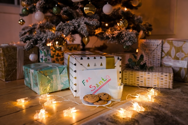 Biscotti fatti in casa e latte con nota alla vigilia di natale sotto l'albero con luci