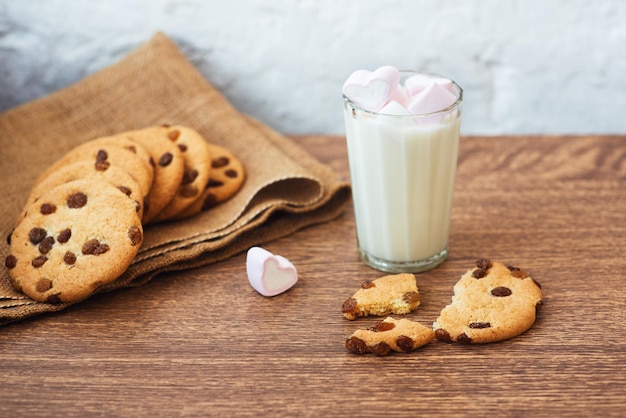 Biscotti fatti in casa fragranti e gustosi con uvetta marshmallow a forma di cuore e un bicchiere di latte fresco sul tavolo