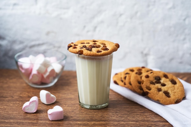 Biscotti fatti in casa fragranti e gustosi con uvetta, marshmallow a forma di cuori e bicchiere di latte fresco sul tavolo