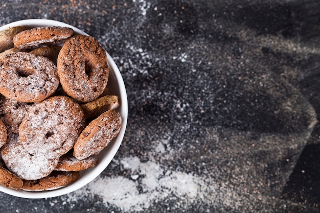 Biscotti freschi di avena e di pepita di cioccolato al forno freschi con il mucchio della polvere dello zucchero in fondo bianco nero della ciotola n