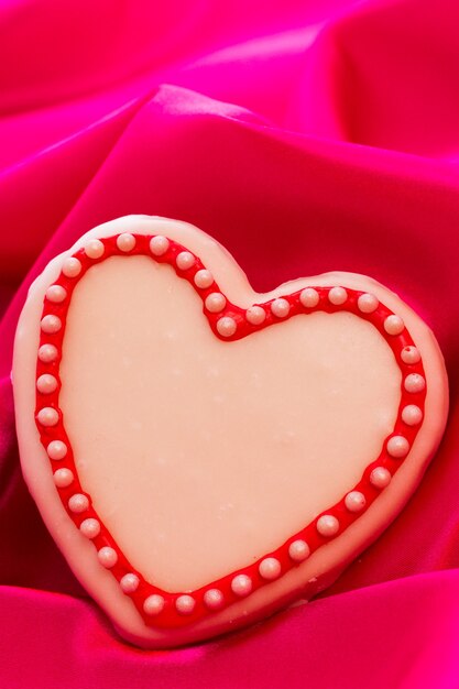 Biscotti gourmet a forma di cuore decorati per San Valentino su seta rosa.