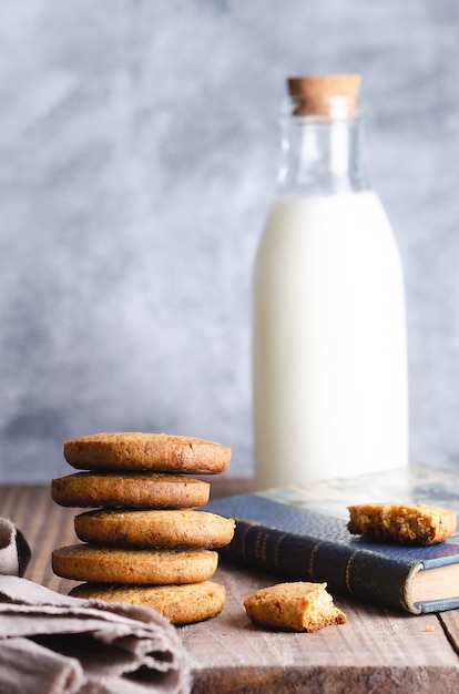 Biscotti impilati e una bottiglia di latte su un libro blu e un tovagliolo beige su un tavolo di legno