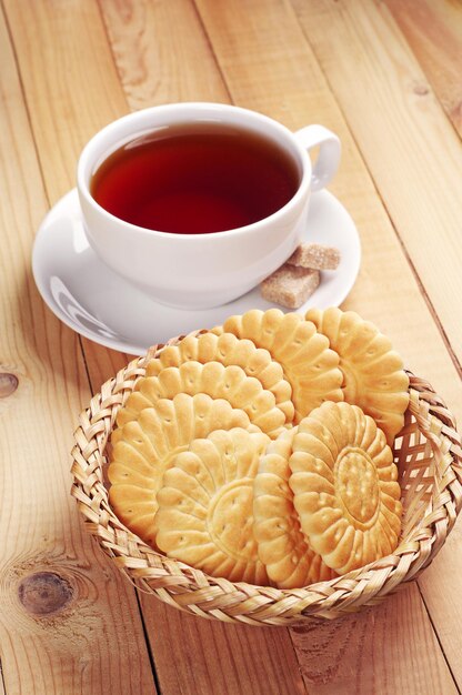 Biscotti in ciotola di vimini e tazza di tè sul tavolo di legno