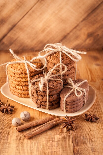 Biscotti integrali fatti in casa con farina d'avena, lino e semi di sesamo e biscotti tradizionali con scaglie di cioccolato su tavolo in legno rustico scuro e spezie.