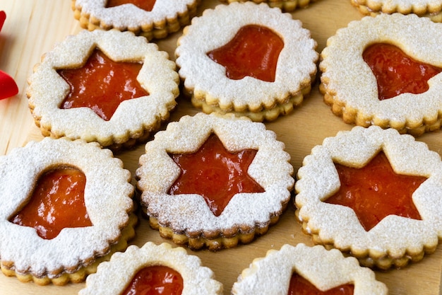 Biscotti linzer di Natale a forma di stelle e campane con marmellata su legno