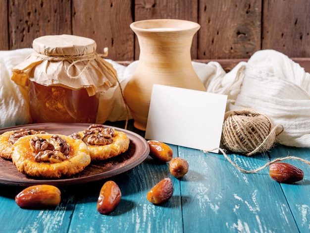 biscotti, miele, datteri, lattiera e carta su legno turchese