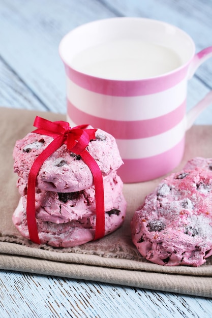 Biscotti rosa e tazza con latte sul primo piano del tavolo