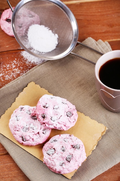 Biscotti rosa e tazza di caffè sul tavolo di legno