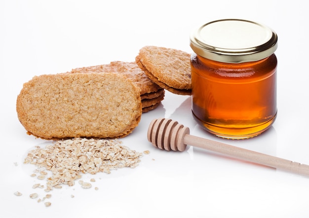 Biscotti sani del chicco di prima colazione della prima colazione con miele e porridge crudo dell'avena su fondo bianco