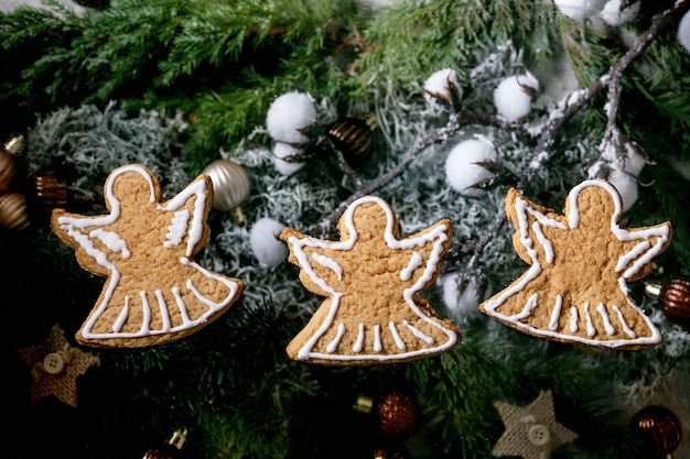 Biscotti tradizionali fatti in casa del pan di zenzero di Natale con glassa decorata. Tre angeli di panpepato con decorazioni natalizie e abete