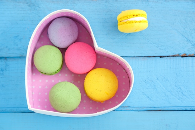 Biscotti variopinti del macaron e una scatola in forma di cuore su un fondo d'annata di legno blu