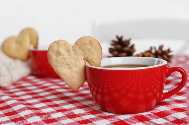 Biscotto a forma di cuore sulla tazza di caffè sul primo piano a quadretti del tovagliolo