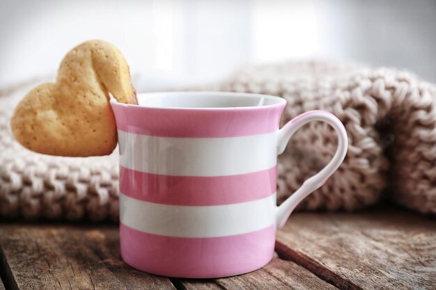 Biscotto a forma di cuore sulla tazza di caffè sul primo piano della tavola di legno