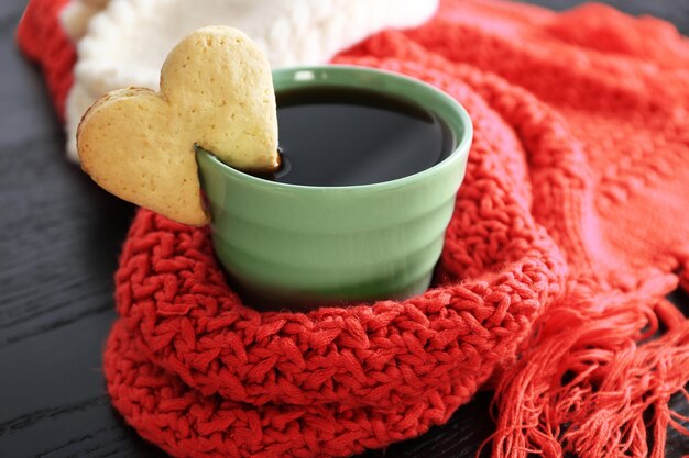 Biscotto a forma di cuore sulla tazza di caffè sul primo piano della tavola di legno