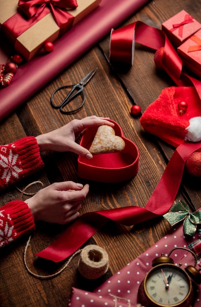 Biscotto di forma del cuore della tenuta della donna sulla tavola di legno nel tempo di avvolgimento