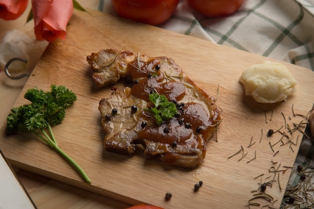 Bistecca alla griglia barbecue di maiale e contorni sul tagliere sul tavolo