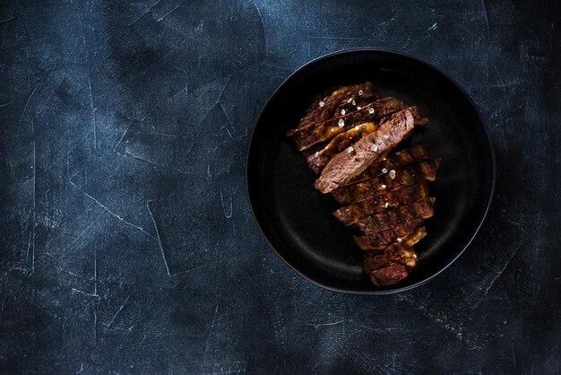 Bistecca alla griglia ben fatta Ribeye in piastra su uno sfondo di cemento scuro